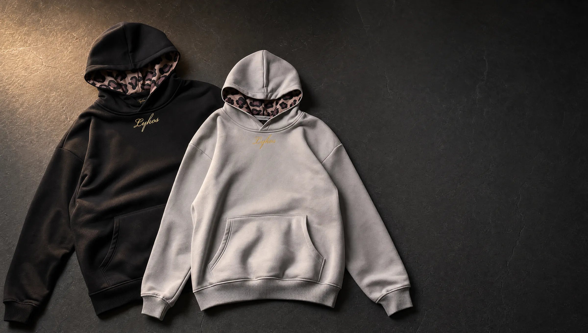 Origin Hoodies in black and grey laid on dark concrete, both hoods showing the leopard lining